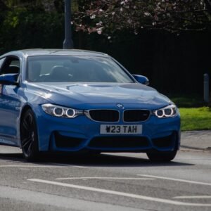Sleek blue sports car driving on a sunny urban road with green surroundings.