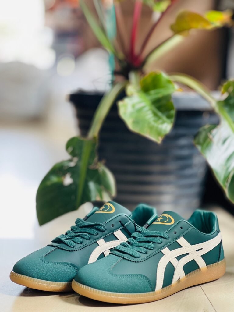Fashionable green sneakers with white stripes beside a potted plant indoors.