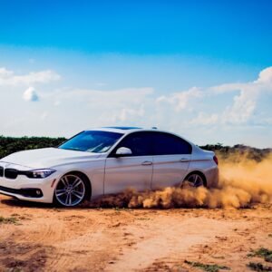 White luxury car drifting on a dirt road, creating a dramatic dust cloud under a blue sky.